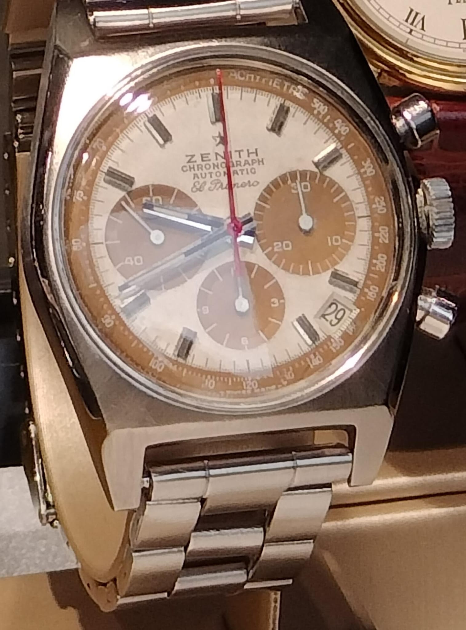 A Zenith El Primero A384 with a silver dial and tan registers on a steel bracelet inside a display case