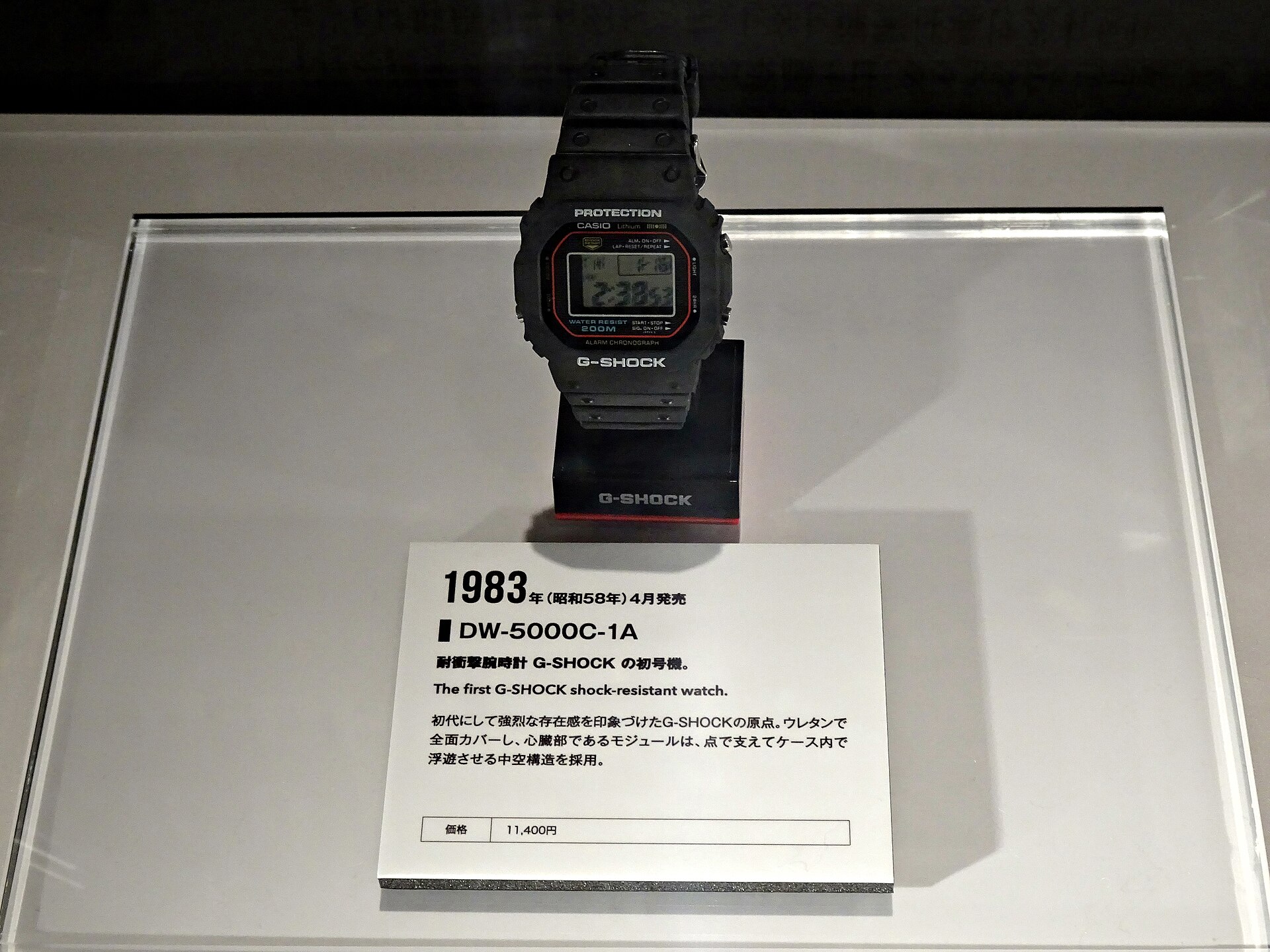 A G-Shock DW-5000C-1A on a museum stand with a Japanese plaque dated April 1983