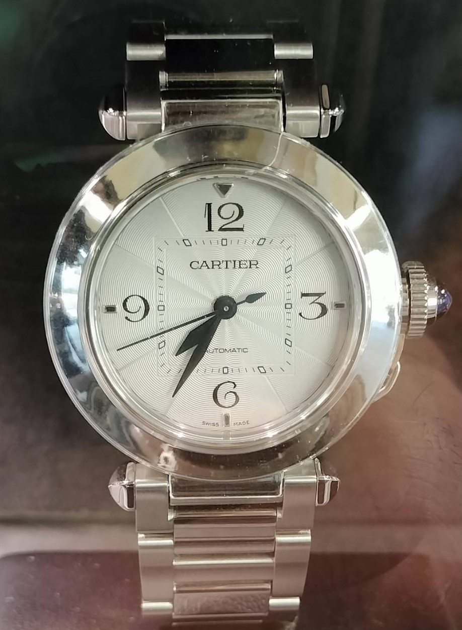 A round steel Pasha de Cartier with Arabic numerals and a capped crown displayed behind glass