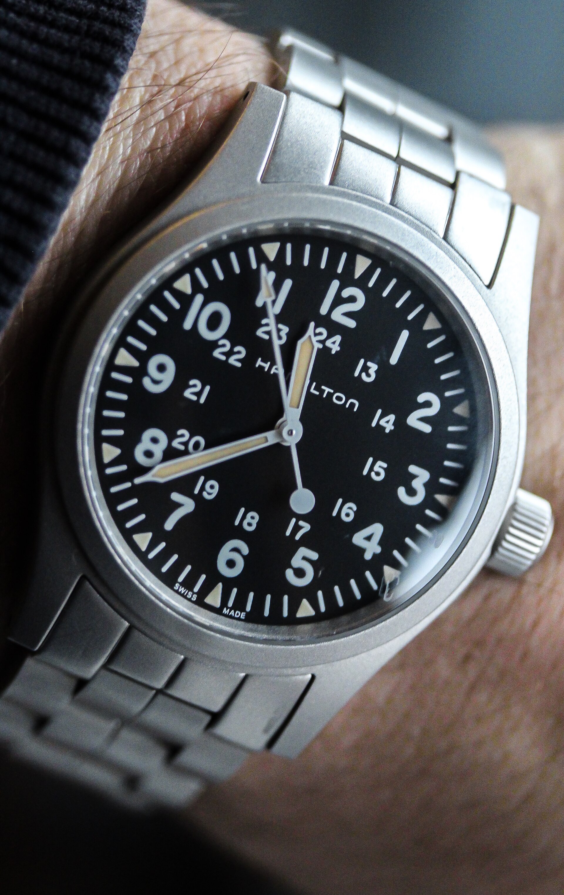 A Hamilton Khaki Field Mechanical with a black dial and 24-hour track on a steel bracelet, worn on a wrist