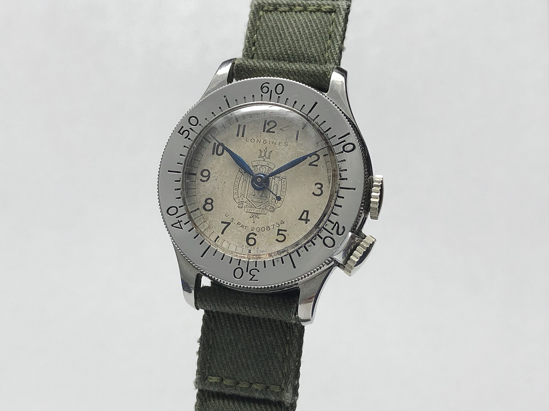 A vintage Longines Weems second-setting watch with a rotating centre disc and a US Naval Academy crest on the dial, on a green strap