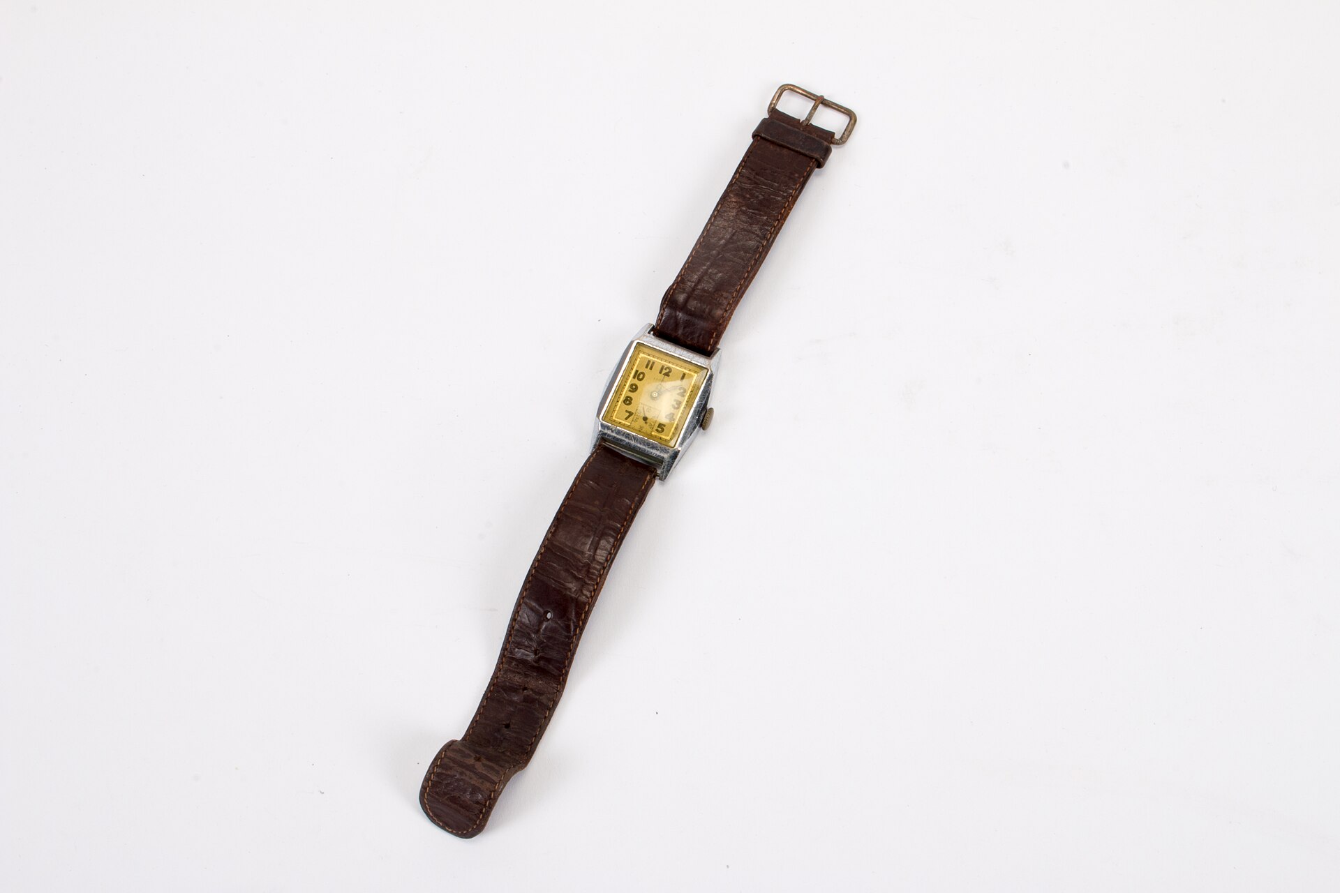 A small square vintage wristwatch with a yellowed dial on a worn brown leather strap, photographed on white