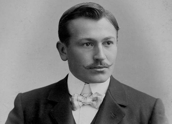 Black-and-white portrait of a young Hans Wilsdorf with a moustache and bow tie