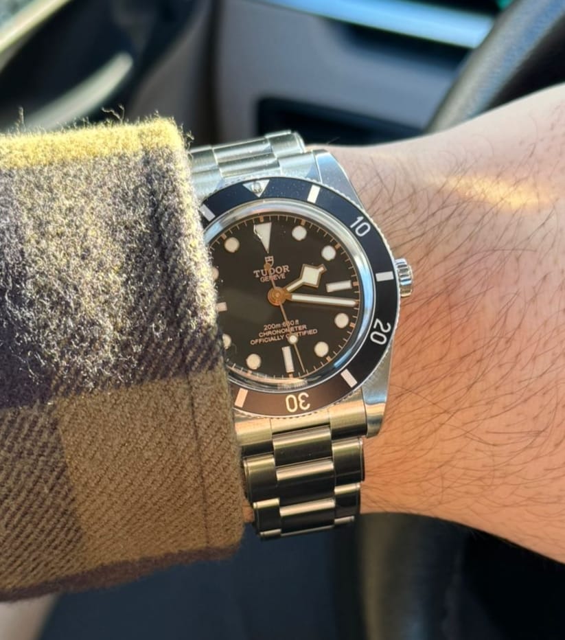 A Tudor Black Bay 54 with black dial and snowflake hands on a wrist under a checked shirt cuff