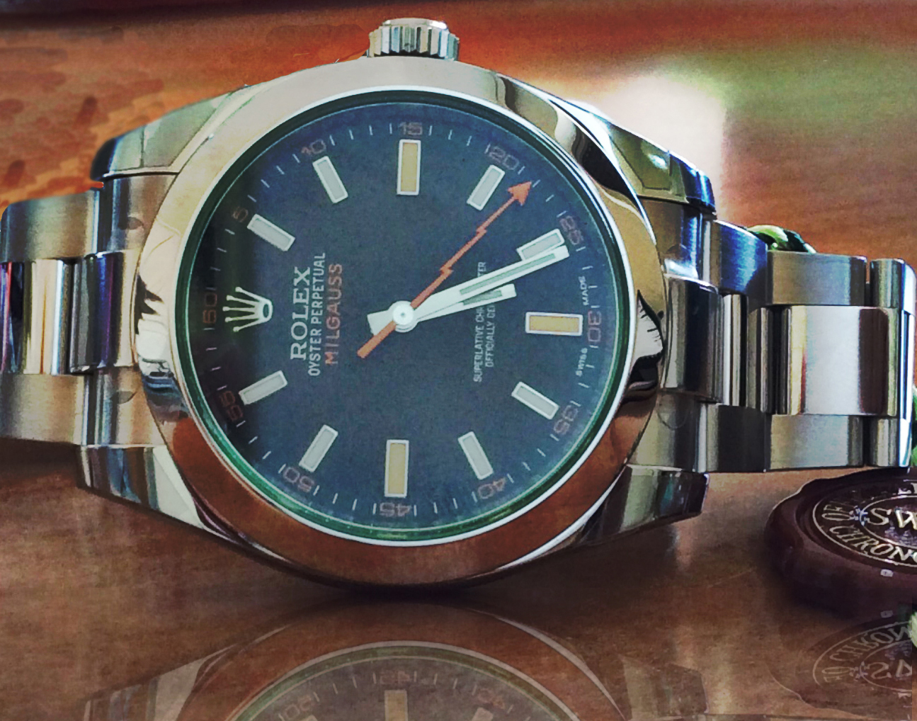 A Rolex Milgauss 116400GV lying on a wooden table, its green-tinted sapphire crystal visible at the edge