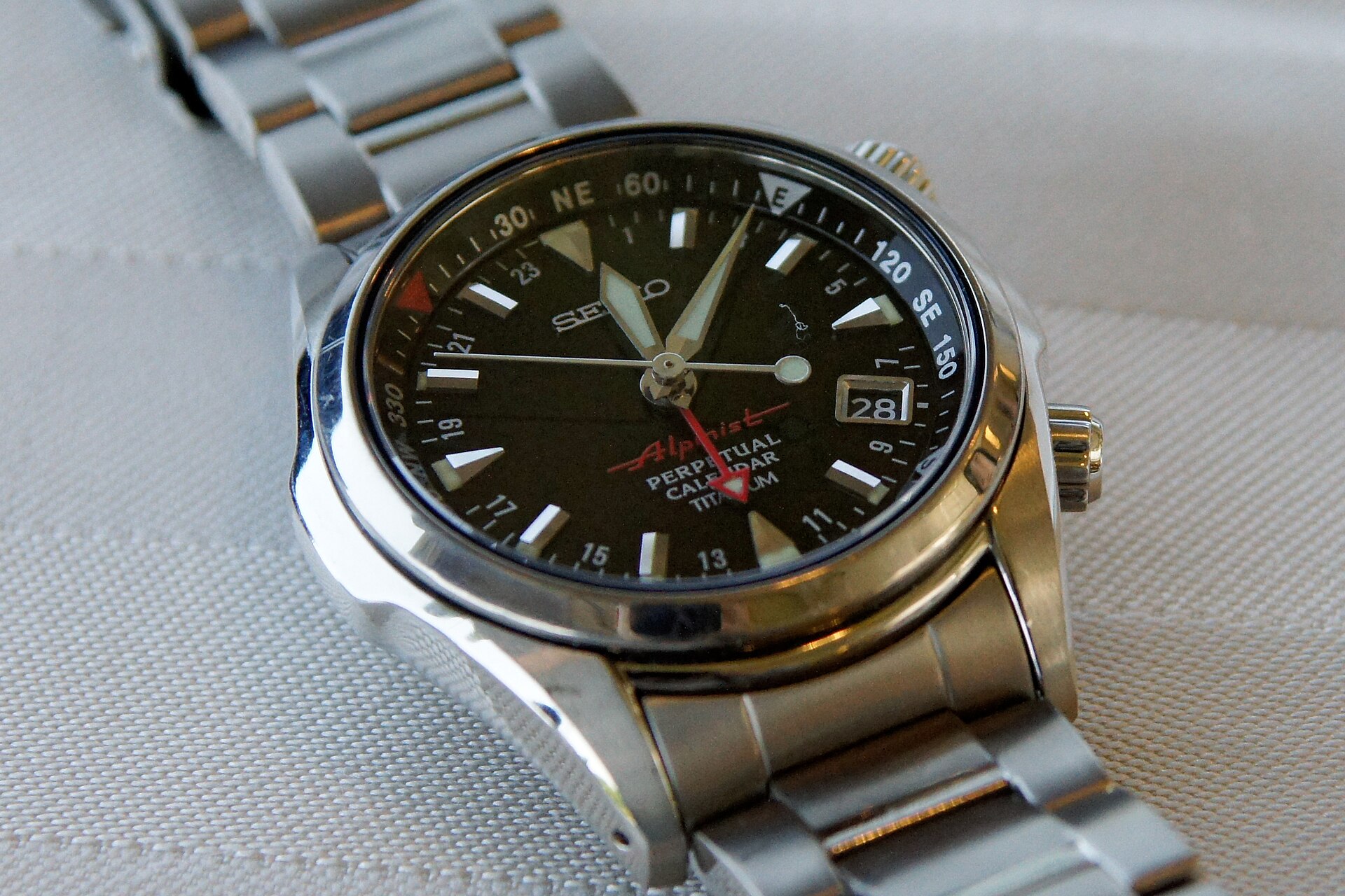 A titanium Seiko Alpinist perpetual calendar with a black dial, red Alpinist script and an internal compass ring