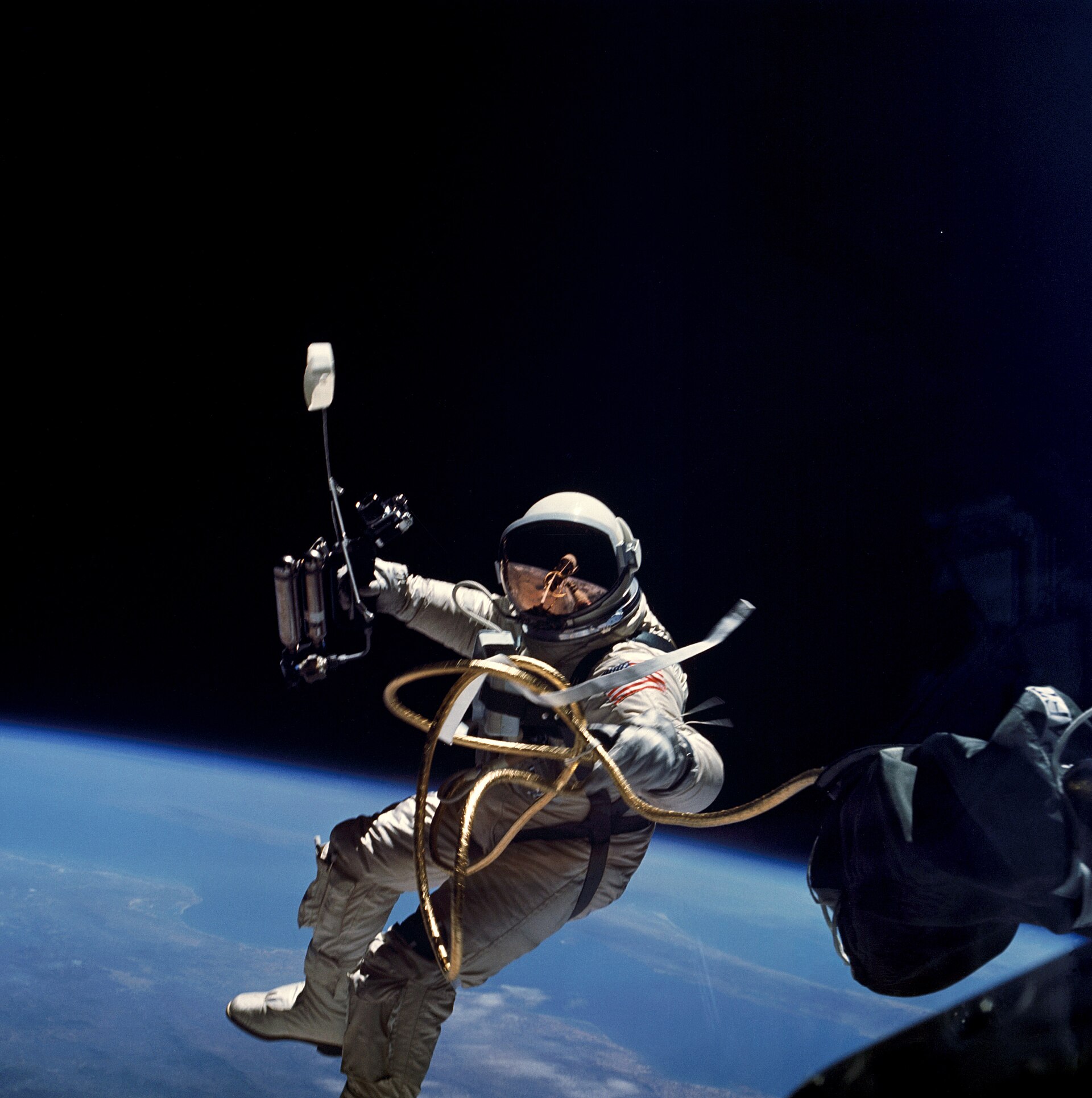 Ed White floating outside Gemini 4 on a gold tether during the first American spacewalk, Earth below