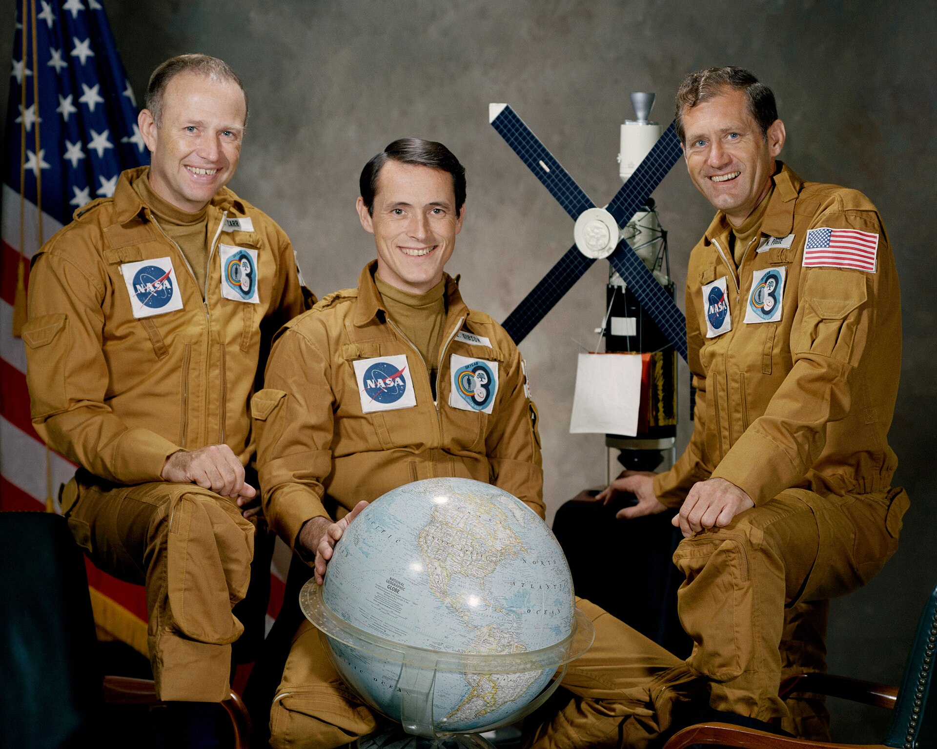Official NASA portrait of the Skylab 4 crew, Gerald Carr, Edward Gibson and William Pogue, in brown flight suits with a globe