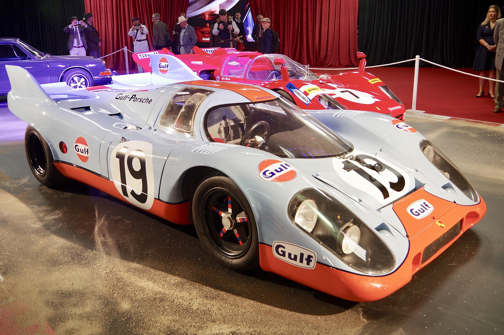 A blue and orange Gulf-liveried Porsche 917K racing car displayed indoors
